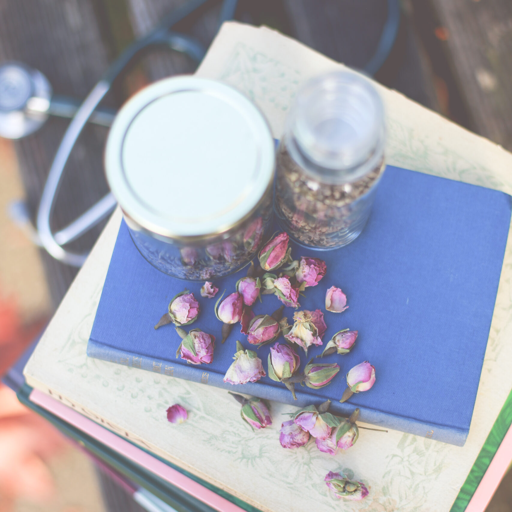 Dried rose buds and herbal remedies on a stack of books with a stethoscope.